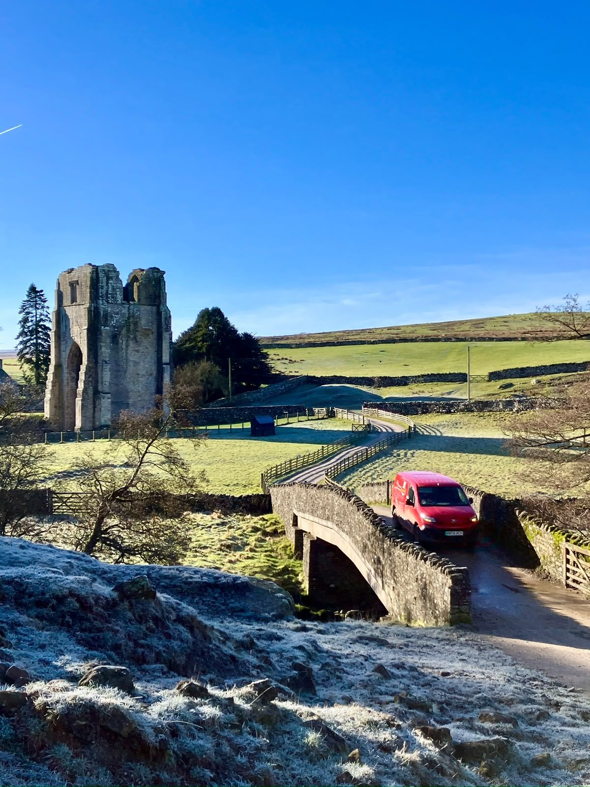 The ruined tower of Shap Abbey on a frosty morning, a red van crossing the bridge.