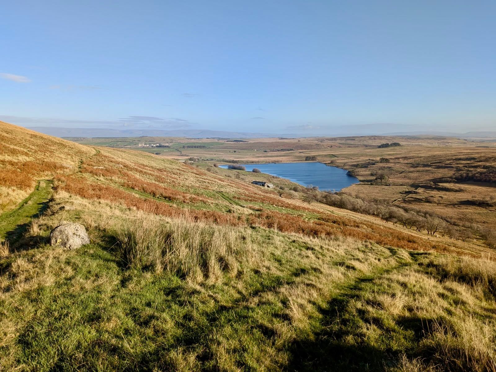 Brown autumn fellside falling away to a blue reservoir far below.